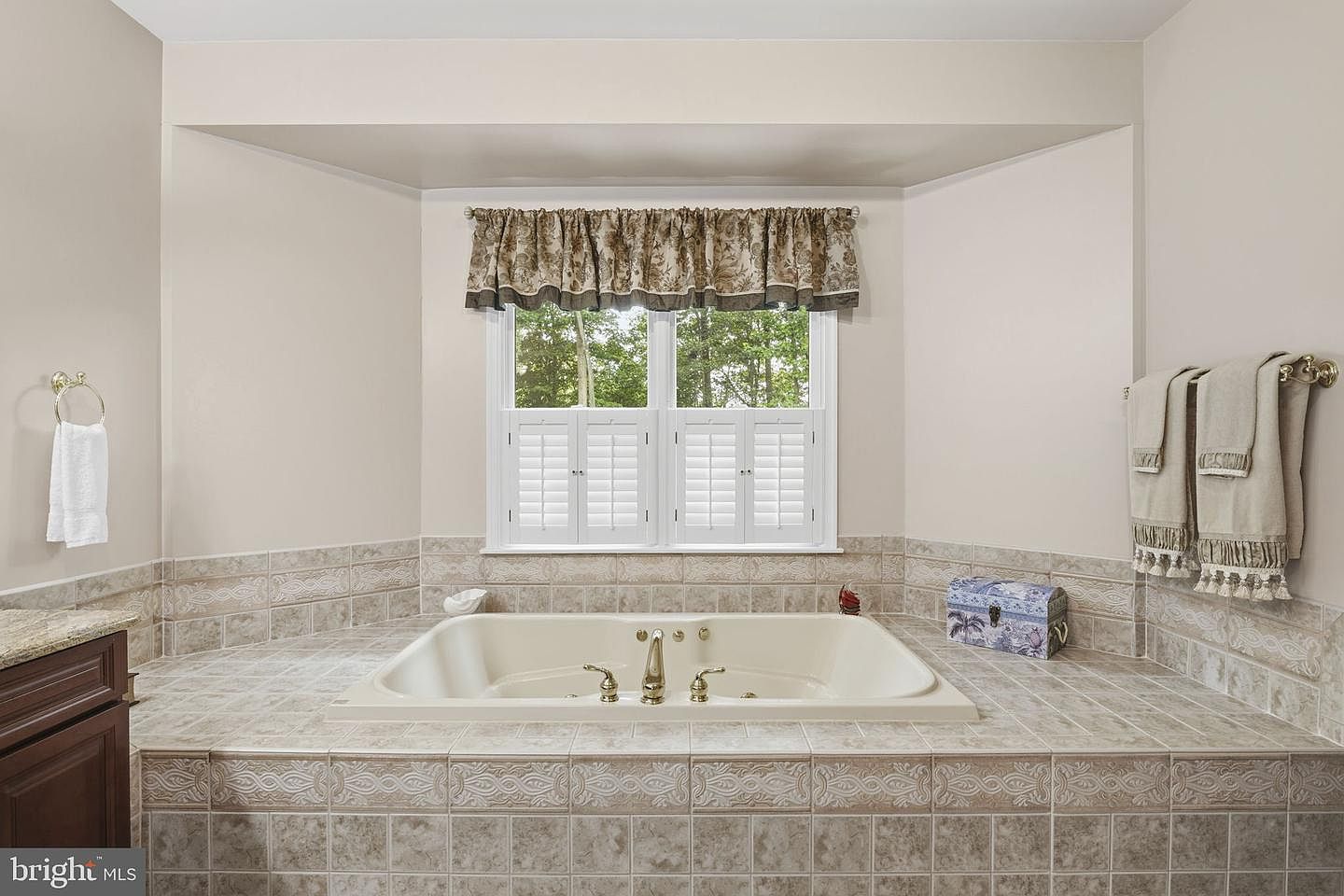 Primary bath with a tiled corner soaking tub and shuttered window