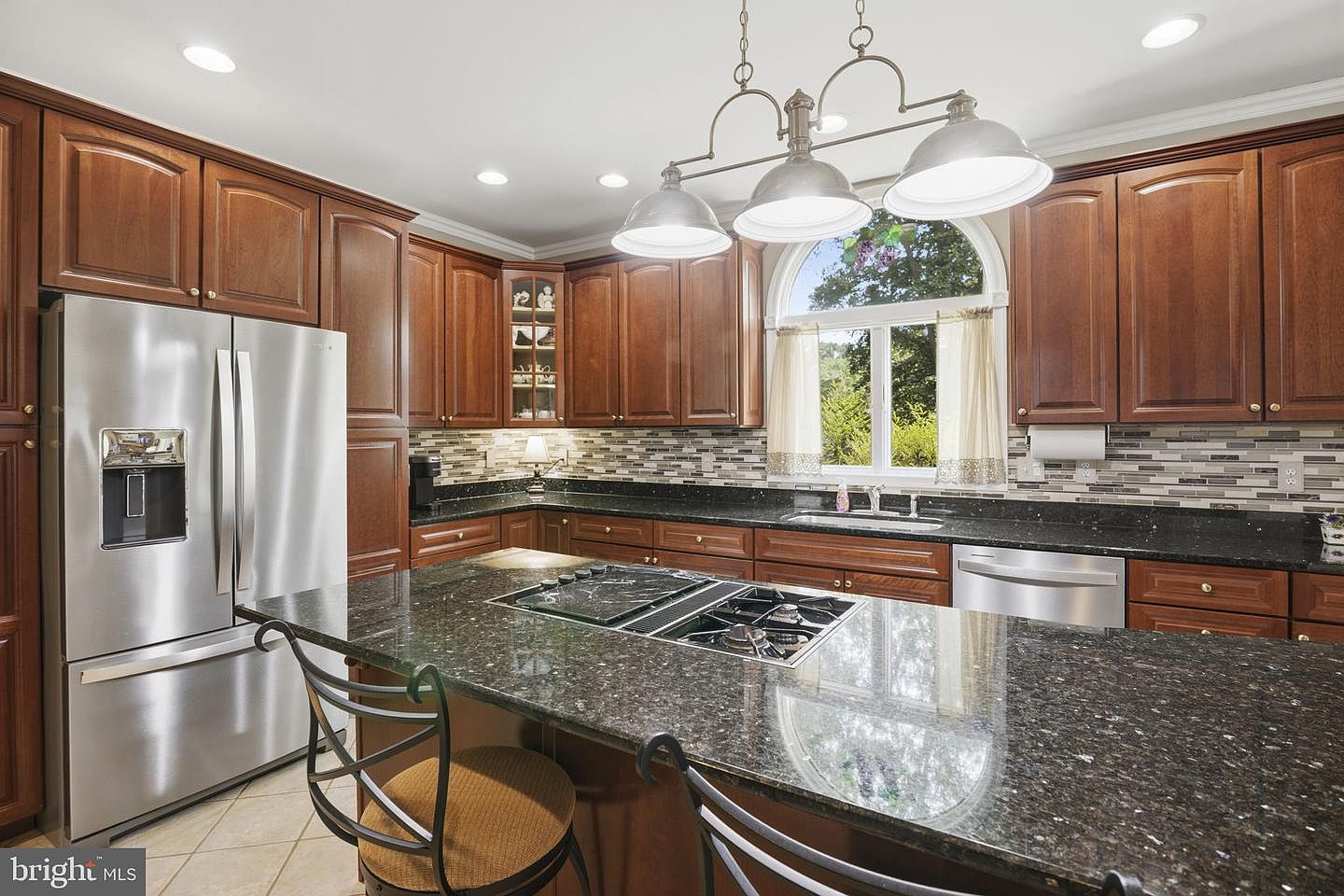 Kitchen island with cooktop, stainless refrigerator and tile backsplash