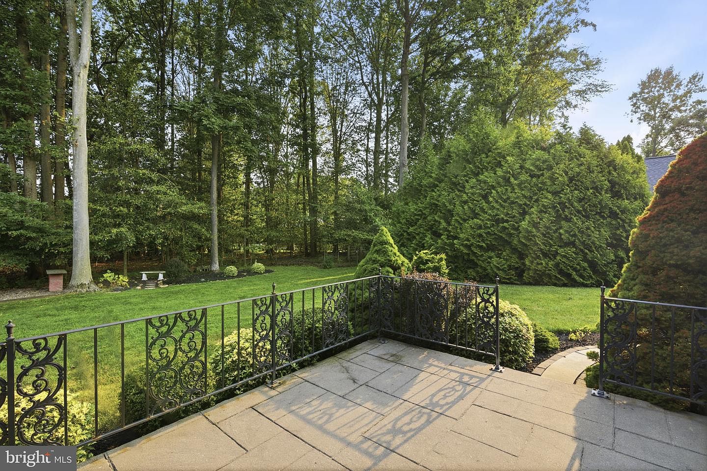 Paver patio with wrought-iron railing overlooking the level, wooded rear yard