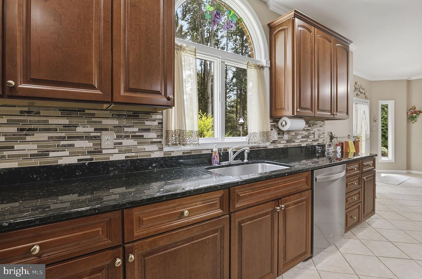 Kitchen sink beneath an arched window with a wooded view